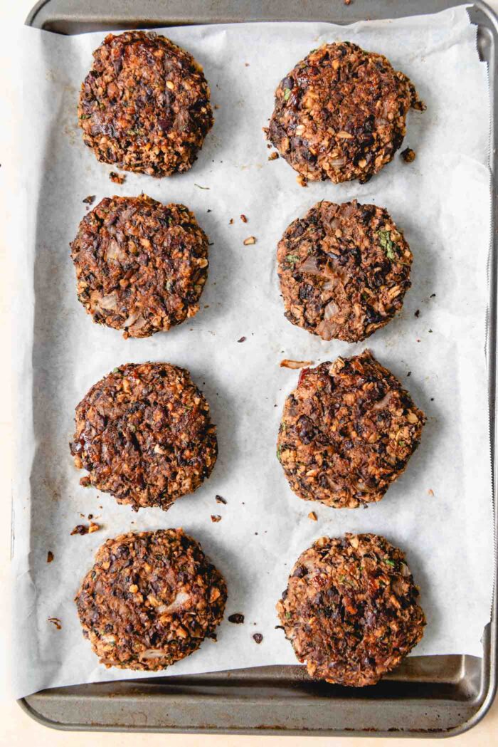 8 baked mushroom veggie burgers on a baking pan lined with parchment paper.