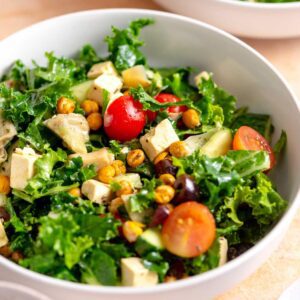 Bowl of kale salad with feta, tomato, cucumber, olives, chickpeas and artichoke hearts.