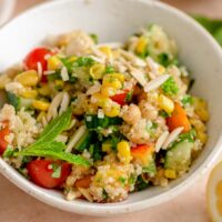 Colourful quinoa salad in a bowl with chickpeas, corn, nectarine, tomatoes, cucumbers and fresh herbs.