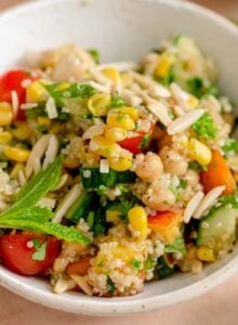 Colourful quinoa salad in a bowl with chickpeas, corn, nectarine, tomatoes, cucumbers and fresh herbs.