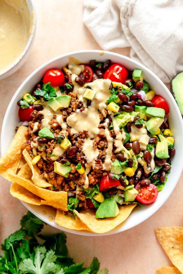 A plant-based taco salad with a mushroom-walnut "meat", lettuce, tomato, onion, black beans, creamy dressing and some tortilla chips on the side.