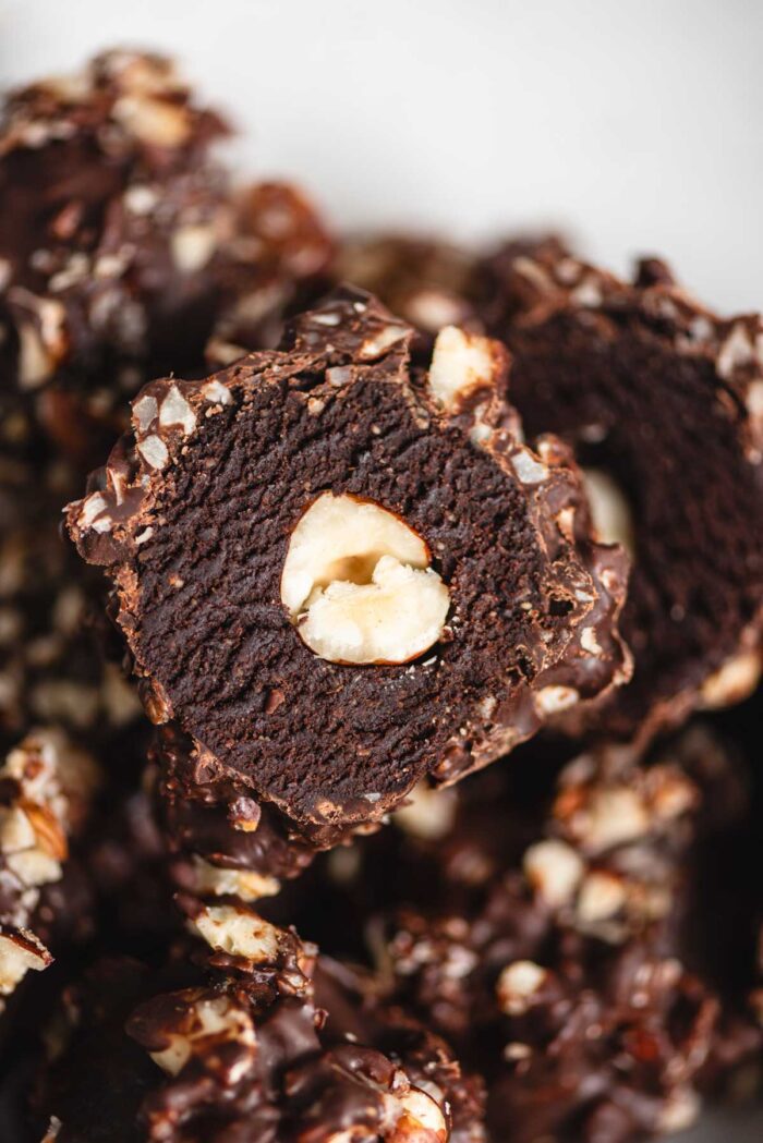 A homemade Ferrero Rocher truffle sliced in half so you can see the texture of the fudge and hazelnut in the middle.
