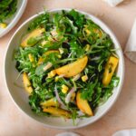 Bowl of arugula peach salad with corn, shallots and almonds.