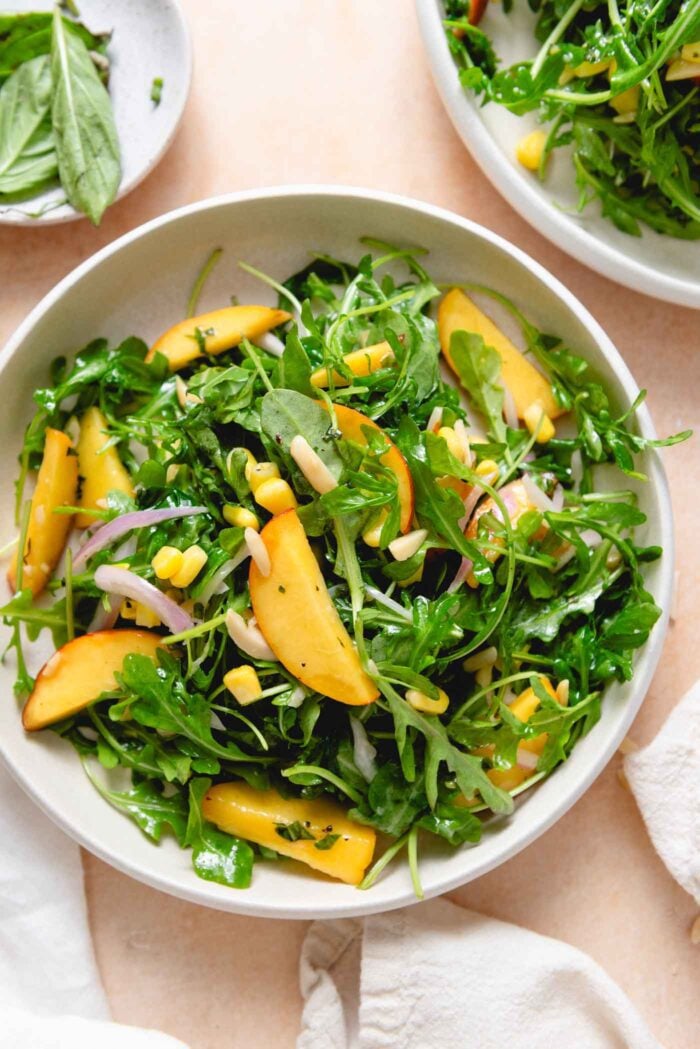 Bowl of arugula peach salad with corn, shallots and almonds.