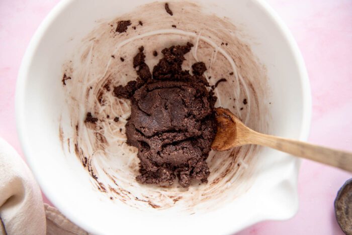 Raw chocolate cookie dough in a glass mixing bowl with a spoon resting in it.