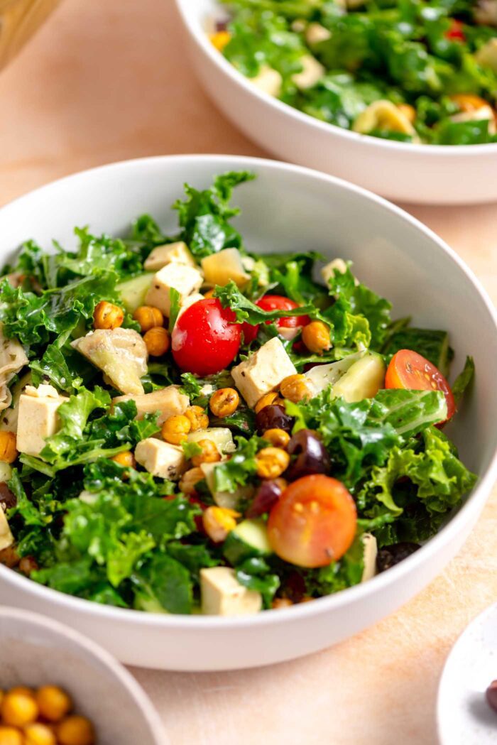 Bowl of kale salad with feta, tomato, cucumber, olives, chickpeas and artichoke hearts.