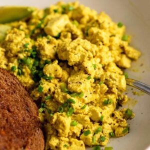 Tofu scramble topped with chopped chives in a bowl with a piece of toast.