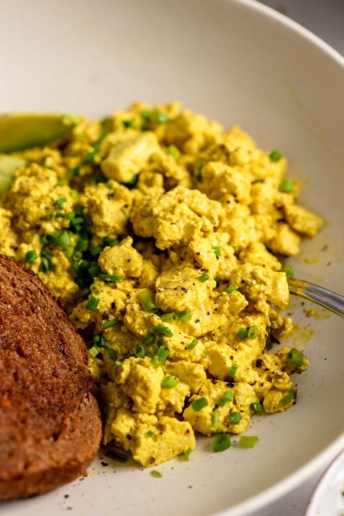 Tofu scramble topped with chopped chives in a bowl with a piece of toast.