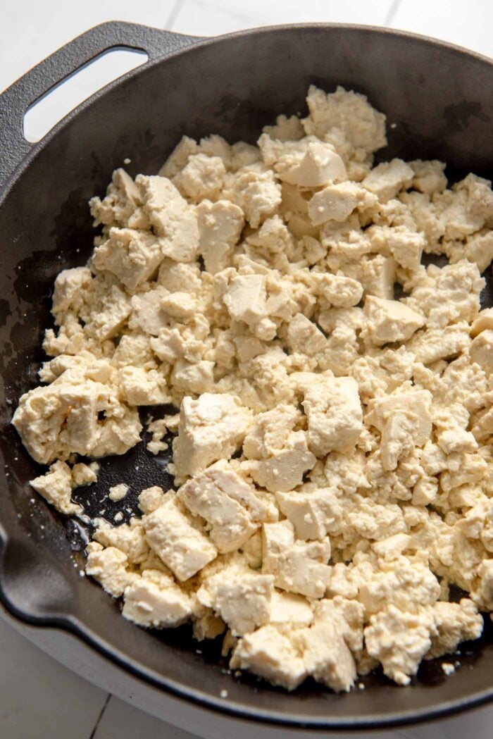 Crumbled tofu bits cooking in a cast iron skillet.