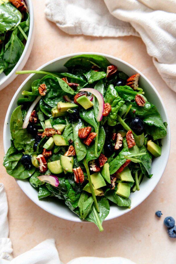 Blueberry spinach salad with sliced red onion, pecans, blueberries and cucumber in a bowl.