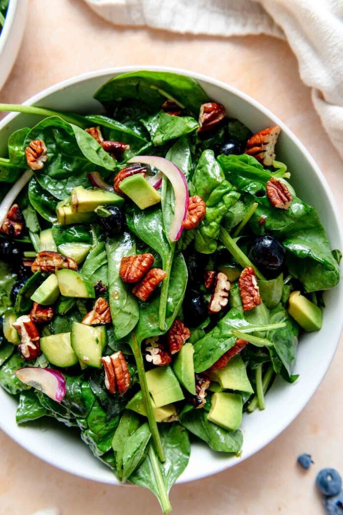 Bowl of blueberry spinach salad topped with candied pecans and diced avocado.