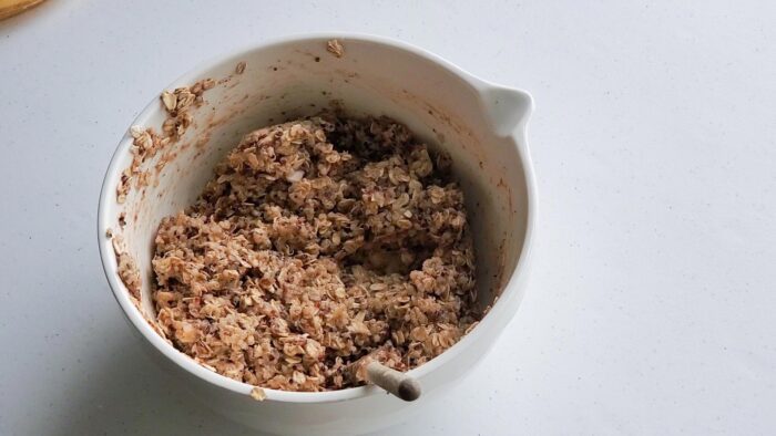 A thick mixture of oats, quinoa and mashed banana in a mixing bowl with a spoon in it.