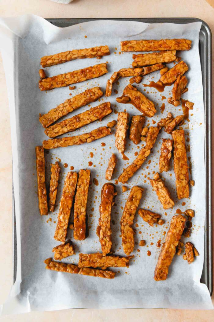 Slices of marinated tempeh spread on a baking sheet lined with parchment paper.