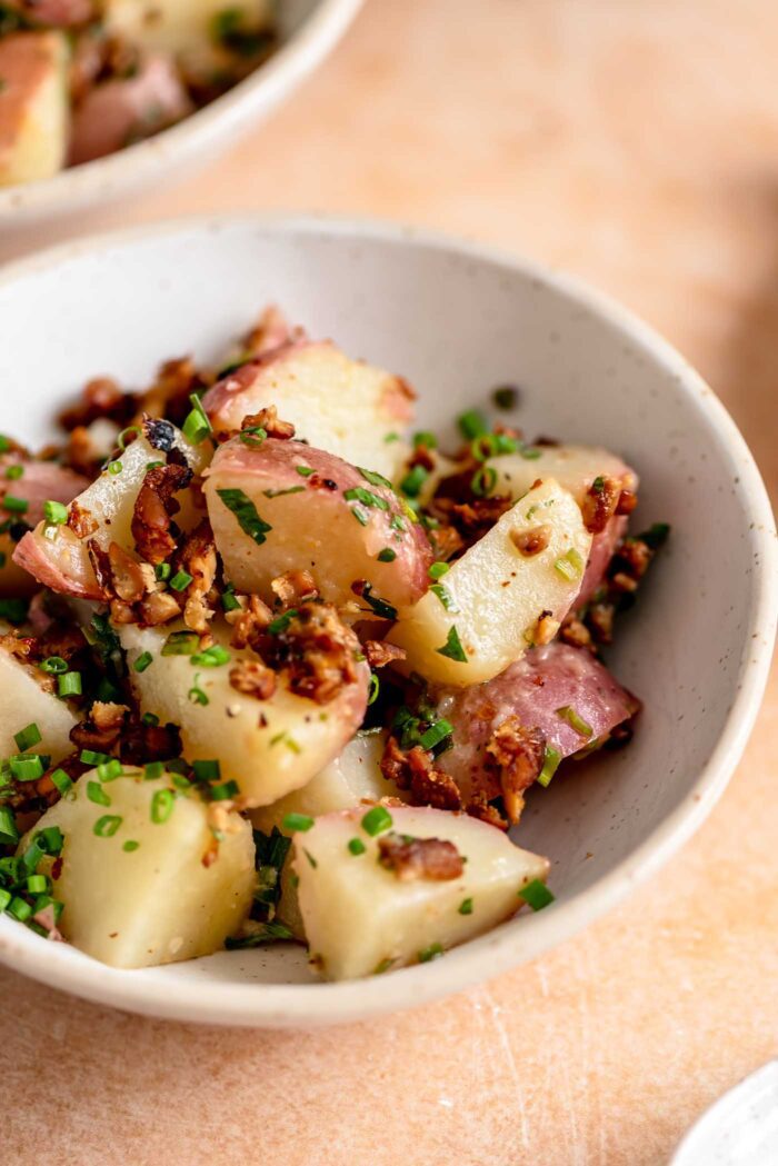 Bowl of warm potato salad with chives, parsley and bacon bits.