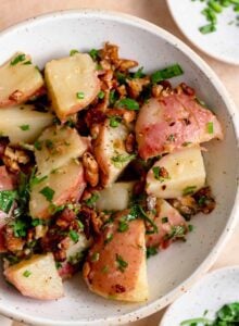 Bowl of warm German potato salad with chives, parsley and bacon bits.