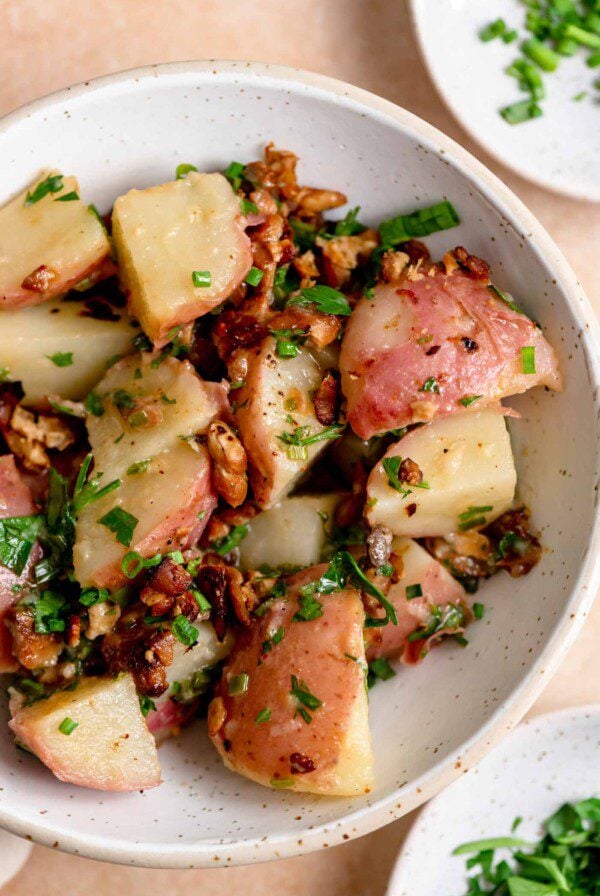 Bowl of warm German potato salad with chives, parsley and bacon bits.