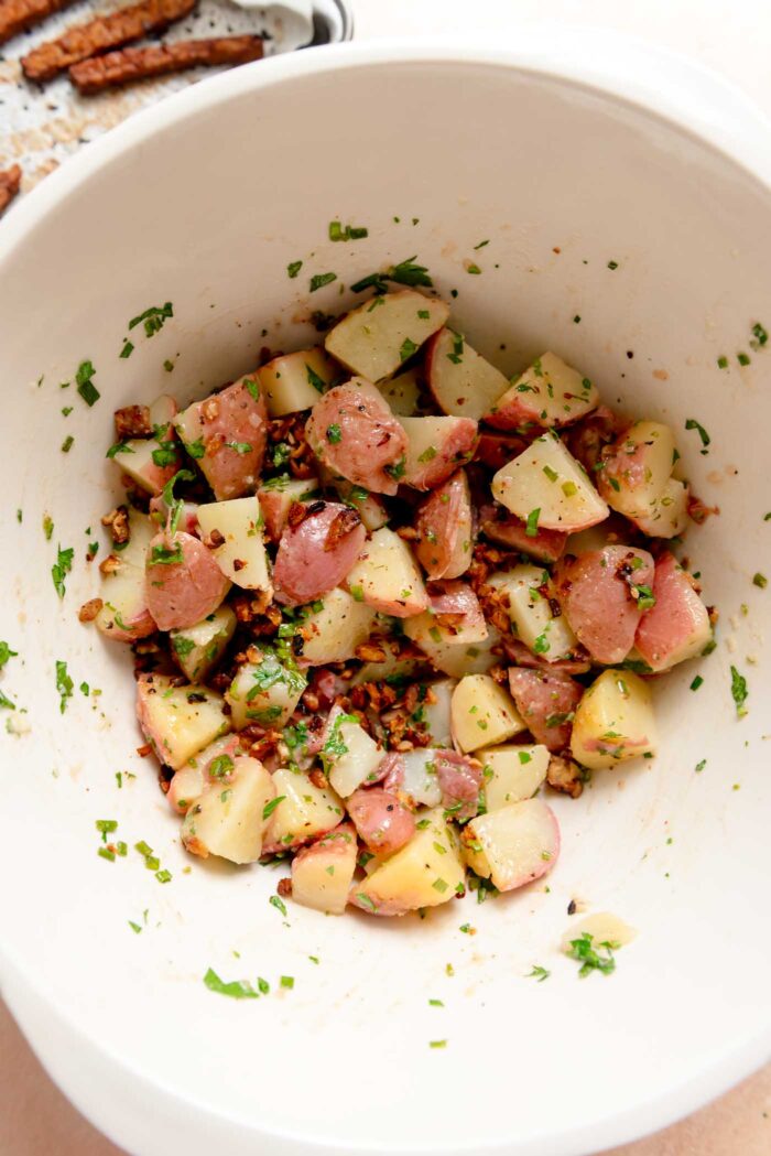 Large mixing bowl of German potato salad with herbs and bacon bits.