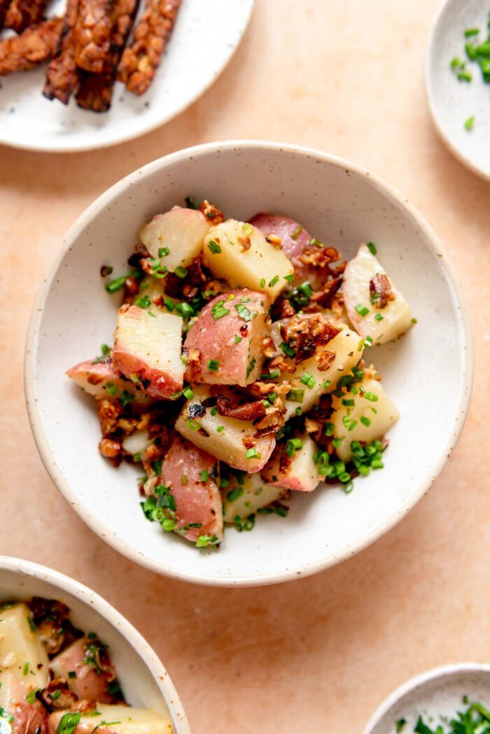 Bowl of hot potato salad made with red potatoes, chives, parsley and tempeh bacon.