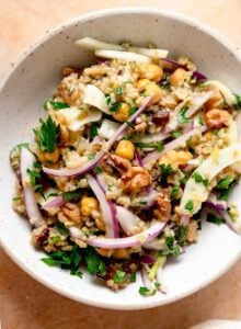 Freekeh salad with red onion, fennel, chickpeas, dates, walnuts and fresh herbs in a serving bowl.