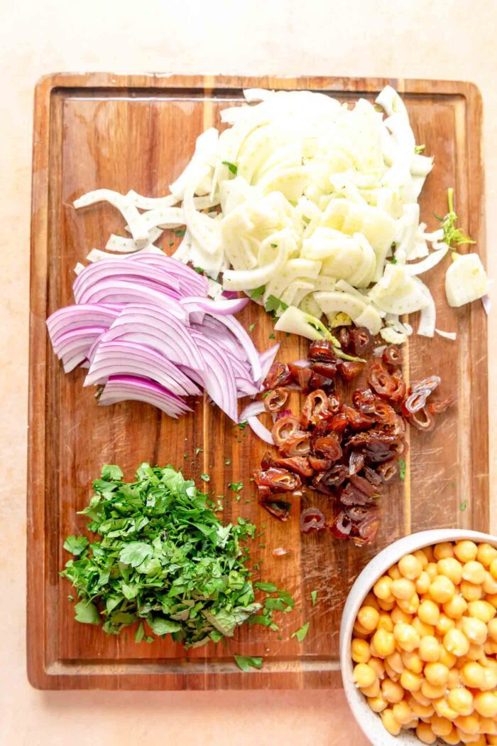 Chopped fennel, mint, parsley, dates and red onion on a cutting board.
