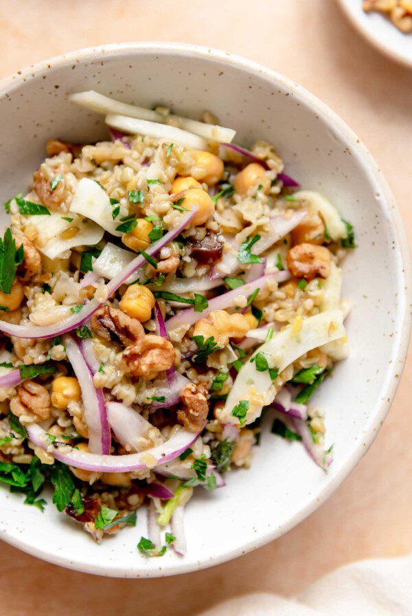 Bowl of freekeh salad with fennel, chickpeas, mint, parsley, dates, red onion and walnuts.