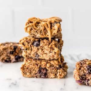 Stack of 3 quinoa and oat baked bars with blueberries, drizzled with peanut buttter.