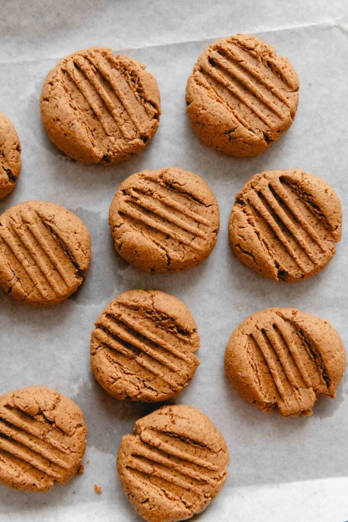 Baked peanut butter cookie with cross-marks on top of them on a baking sheet.