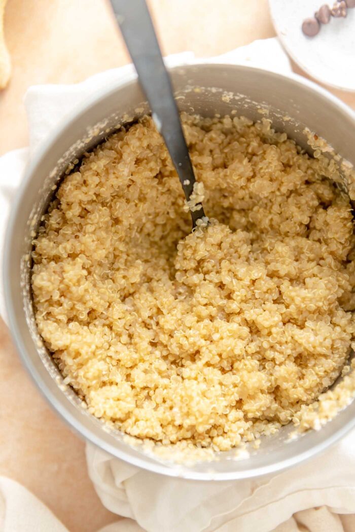 Cooked quinoa in a saucepan with a spoon in it.