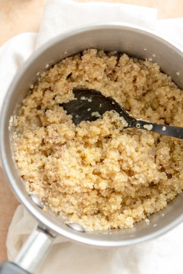 Cooked quinoa in a saucepan with some milk and a spoon resting in it.