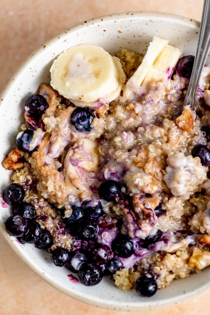 Bowl of breakfast quinoa with blueberries, banana, yogurt, walnut and peanut butter.