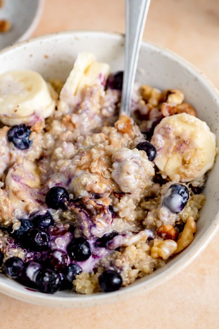 Bowl of breakfast quinoa with blueberries, banana, yogurt, walnut and peanut butter.