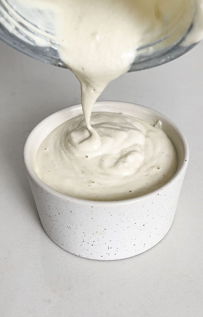 Pouring creamy sauce from a blender container into a small dish.