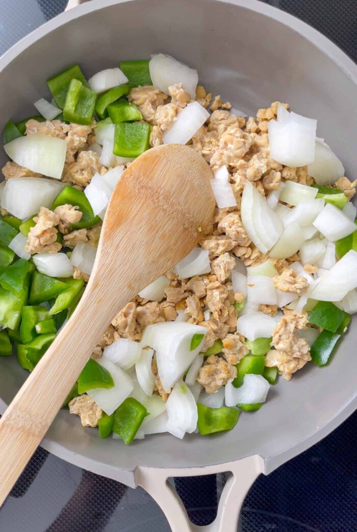 Chopped onion, bell pepper and crumbled tempeh cooking in a pan.