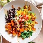 Breakfast burrito bowl with cilantro, tofu scramble, black beans, roasted sweet potato, chipotle sauce and hot sauce drizzled over top.