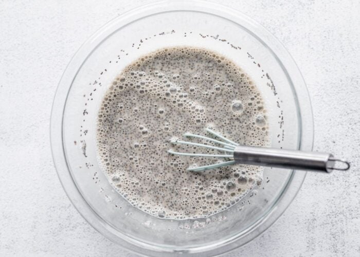 Glass bowl of chia seed pudding with a whisk in it.