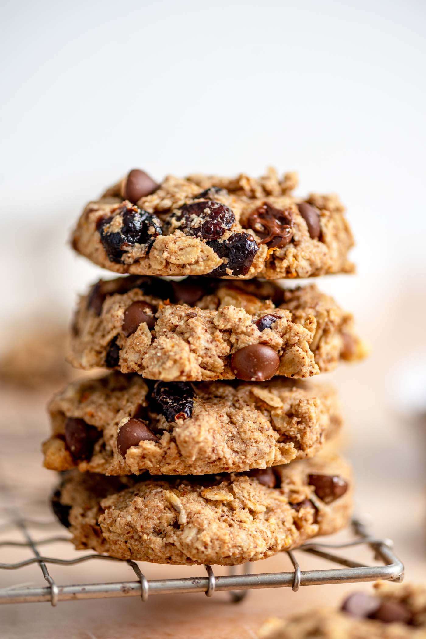Stack of 4 oatmeal cookies with cranberries, walnuts and chocolate chips in them sitting on the edge of a wire baking rack.