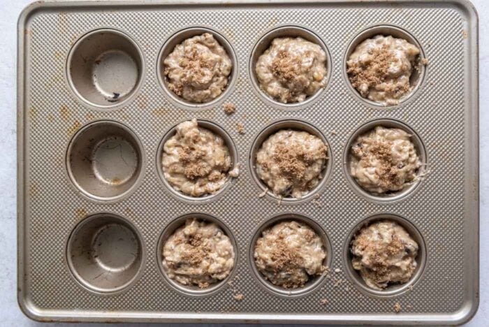 Raw muffin batter topped with brown sugar in a muffin pan.