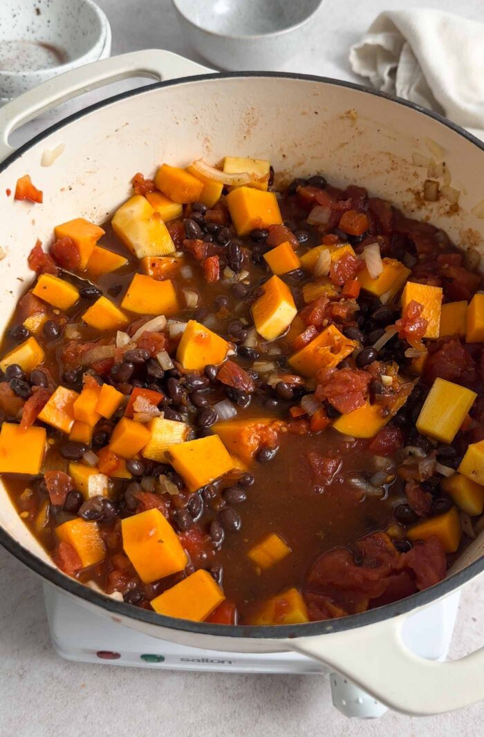 Cubed butternut squash, tomatoes and black beans cooking in a tomato broth in a large soup pot.