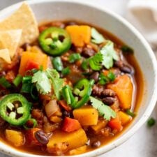 A bowl of butternut squash chili topped with jalapeno, green onion and chips.