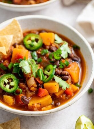 A bowl of butternut squash chili topped with jalapeno, green onion and chips.