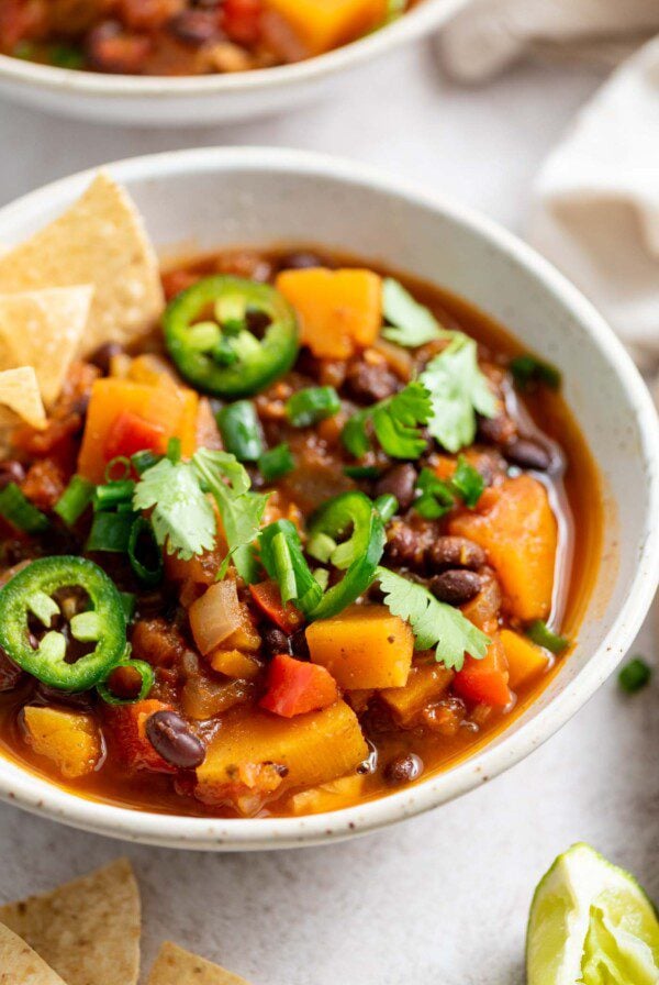 A bowl of butternut squash chili topped with jalapeno, green onion and chips.