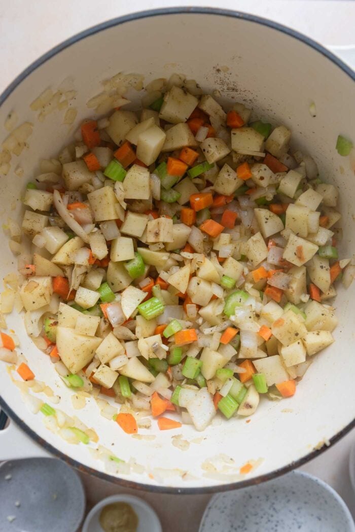 Potato, carrot, celery, onion and herbs cooking in a pot.