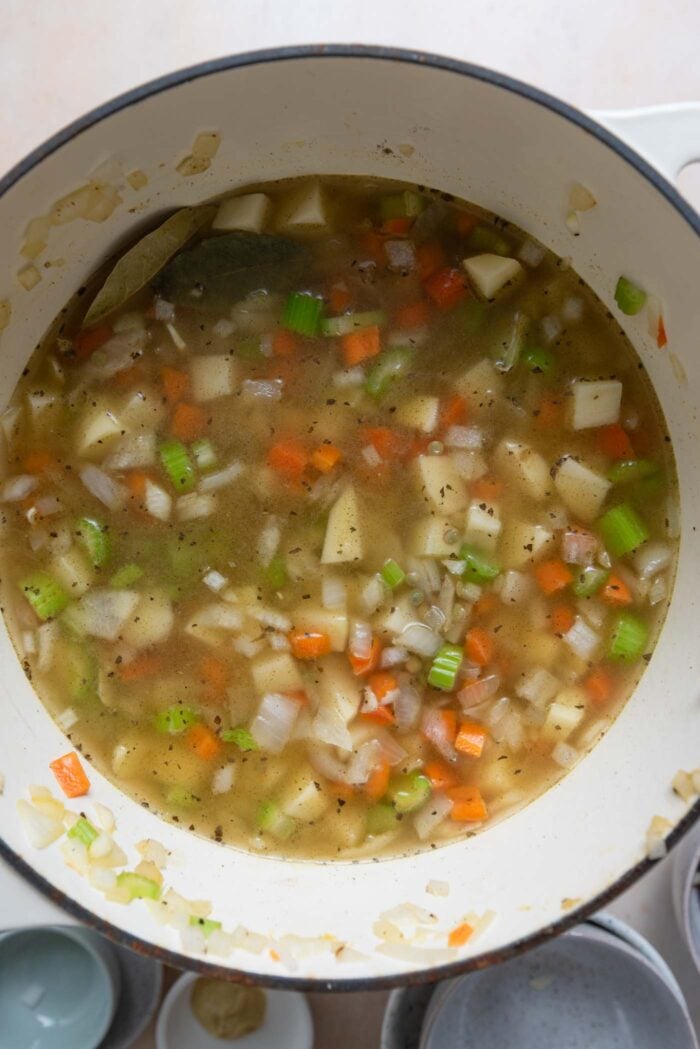 Chopped celery, potato, carrot and onion cooking in broth in a pot.