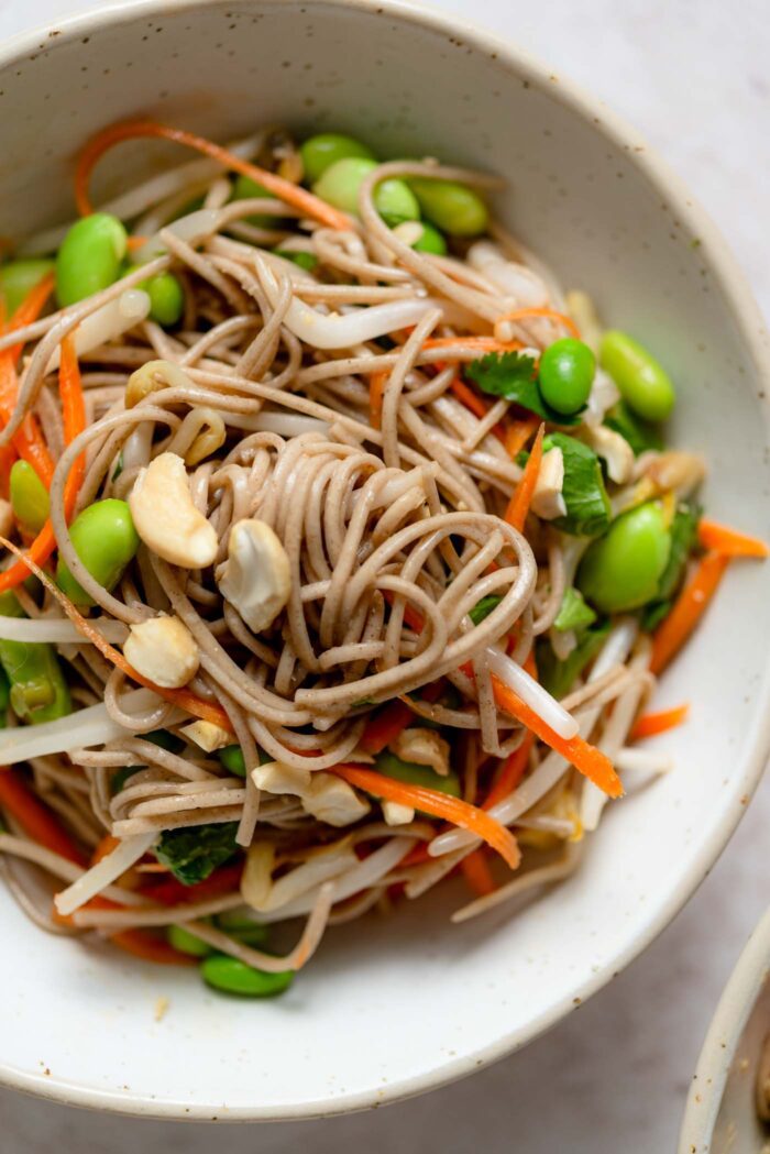 Bowl of soba noodles with edamame, cashews, carrot and bean sprouts.