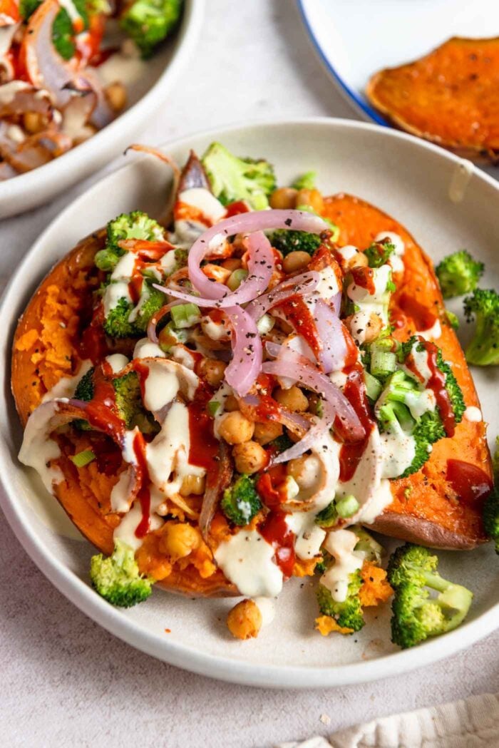 Two halves of a sweet potato topped with broccoli, chickpeas, red onion and tahini sauce.