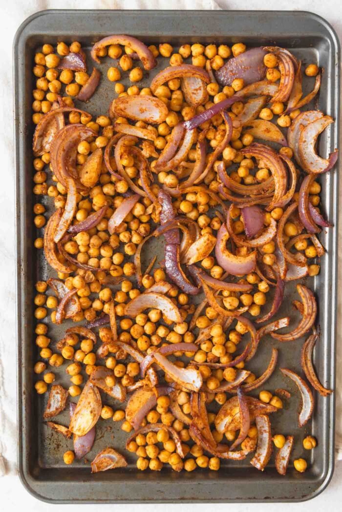 Chickpeas and red onion in spices on a baking sheet.