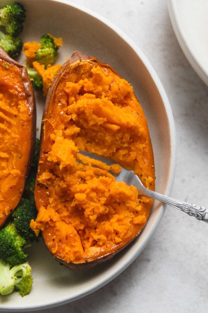 Roasted sweet potato half being mashed with a fork on a plate.