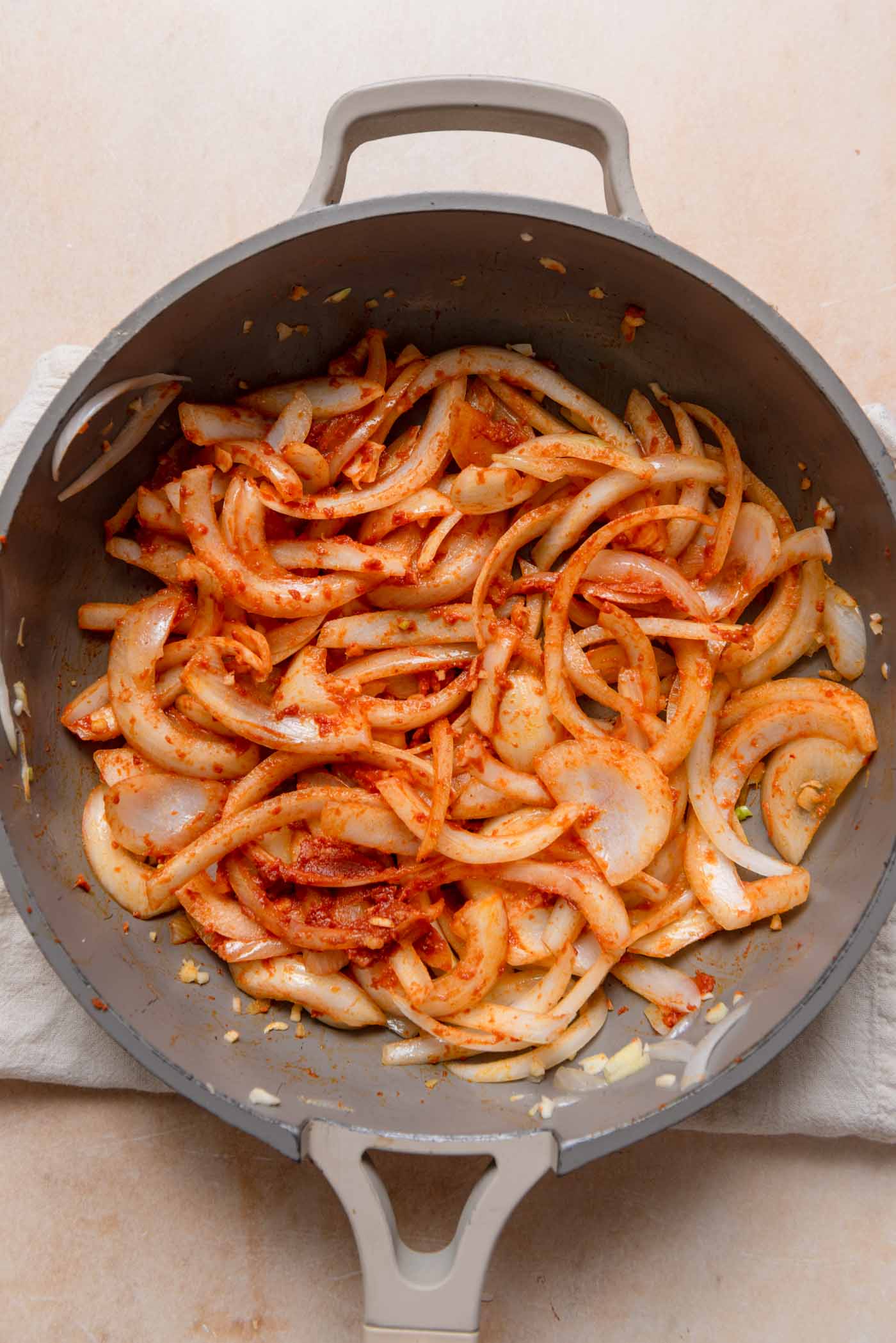 Sliced onions cooking in red curry paste in a pan.