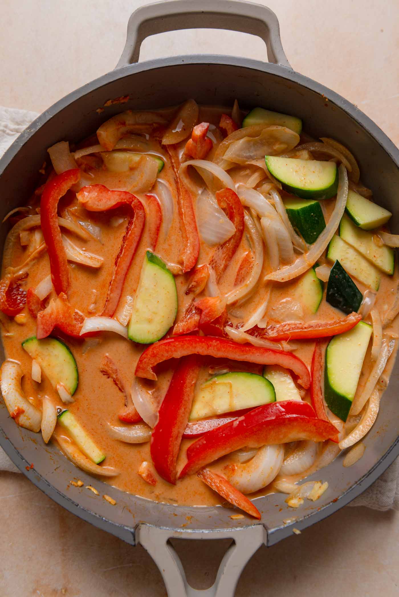 Red curry with vegetables, onion and zucchini cooking in a pan.