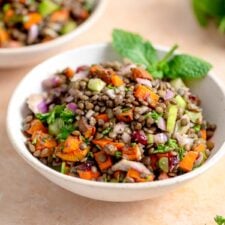 French lentil salad with fresh herbs, sweet potato and diced vegetables in a bowl garnished with fresh mint leaves.